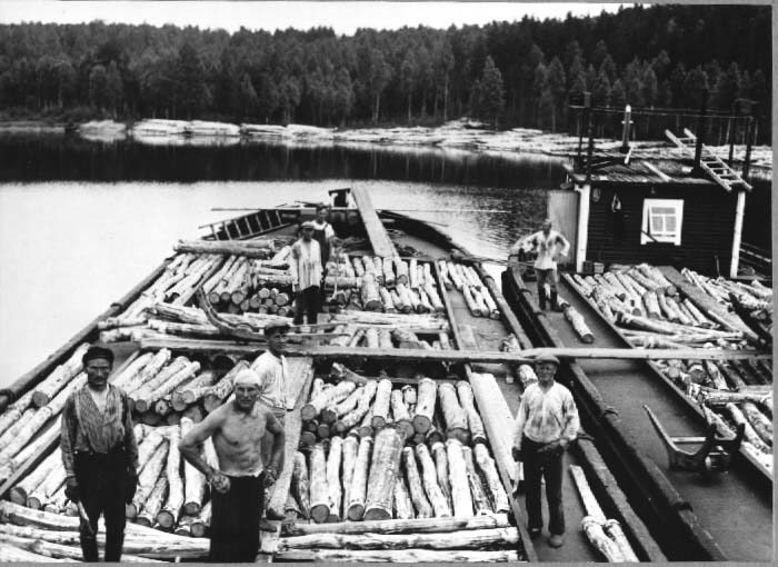 Propsien lastausta lotjiin. Mustavalkoisessa kuvassa näkymä kahteen lotjaan. Kuvassa seisoo kaksi miehistön jäsentä, ja käynnissä propsin eli pienimittaiseksi sahatun puutavaran lastaus lotjien ruumaan.