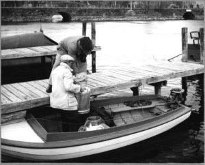 Mies ja poika lastaavat tyhjiä maitotonkkia Savonlinnan kaupungin Puistokadun laiturissa olevaan perämoottoriveneeseen 1950-luvulla.