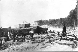 Kangassaaren lotjavarvi eli lotjaveistämö joskus 1919-34. Suomalainen Puuliike Oy:n toimesta vuosina 1919-1934 tapahtunutta laivanrakennusta Enonkosken Kangassaaressa. Kuvassa mestari Emil Bilund, Olli Muhonen, Paavo Tynkkynen, Kalle Kuvaja, Nikodeemus Karjalainen, Jalmari Huoman, Heikki Huoman ja Eemil Huoman.