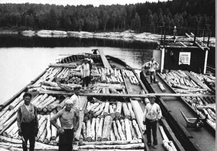 Propsien lastausta lotjiin. Mustavalkoisessa kuvassa näkymä kahteen lotjaan. Kuvassa seisoo kaksi miehistön jäsentä, ja käynnissä propsin eli pienimittaiseksi sahatun puutavaran lastaus lotjien ruumaan.