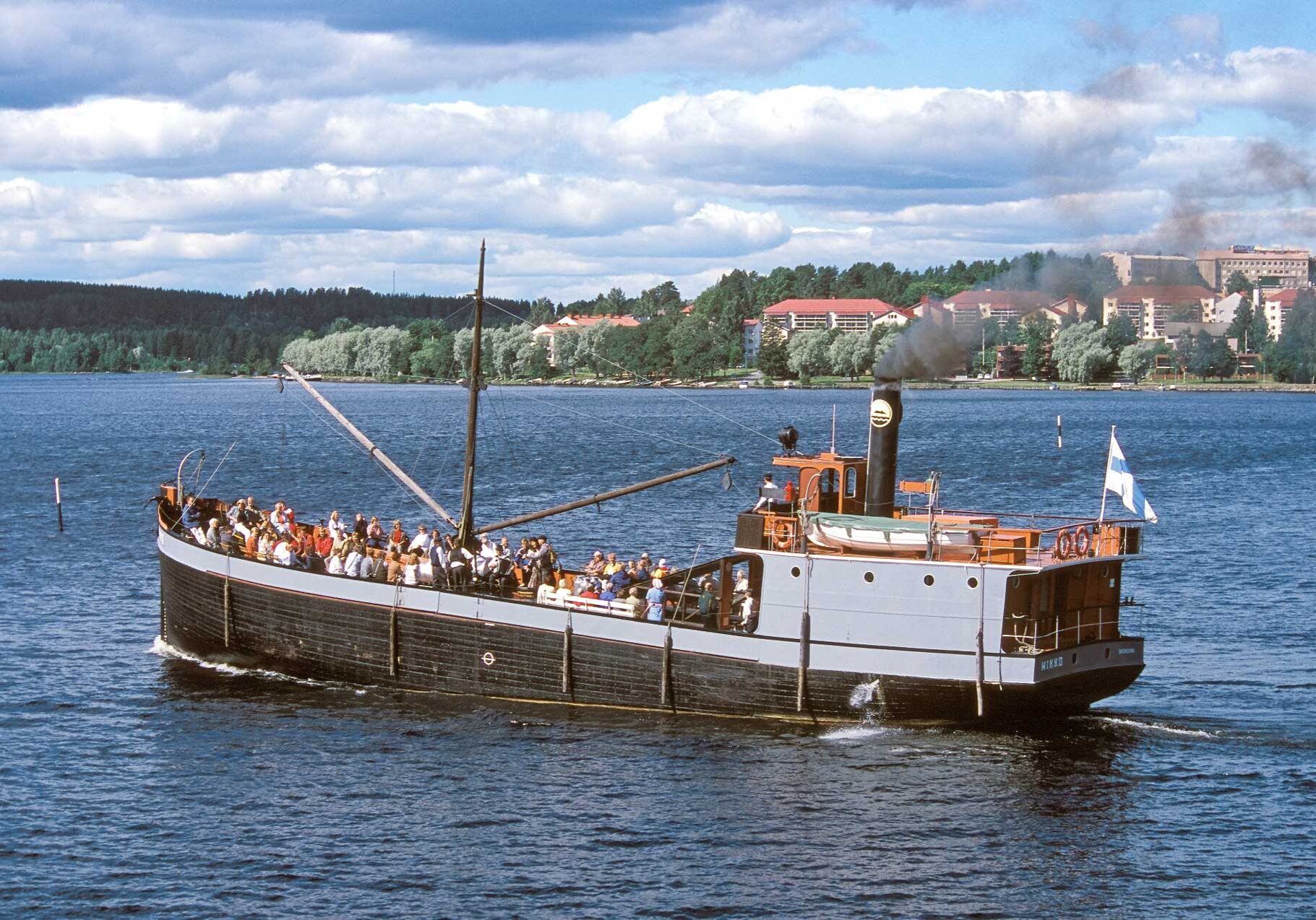 Mikko-laiva Savonlinnan kaupungin vesillä. Taustalla Heikinpohjan kaupunginosa. Kuvassa Mikko-laiva purjehtii kesäisessä maisemassa Savonlinnan kaupungin vesillä. Kuvassa taustalla näkyy Savonlinnan Heikinpohjan kaupunginosa.