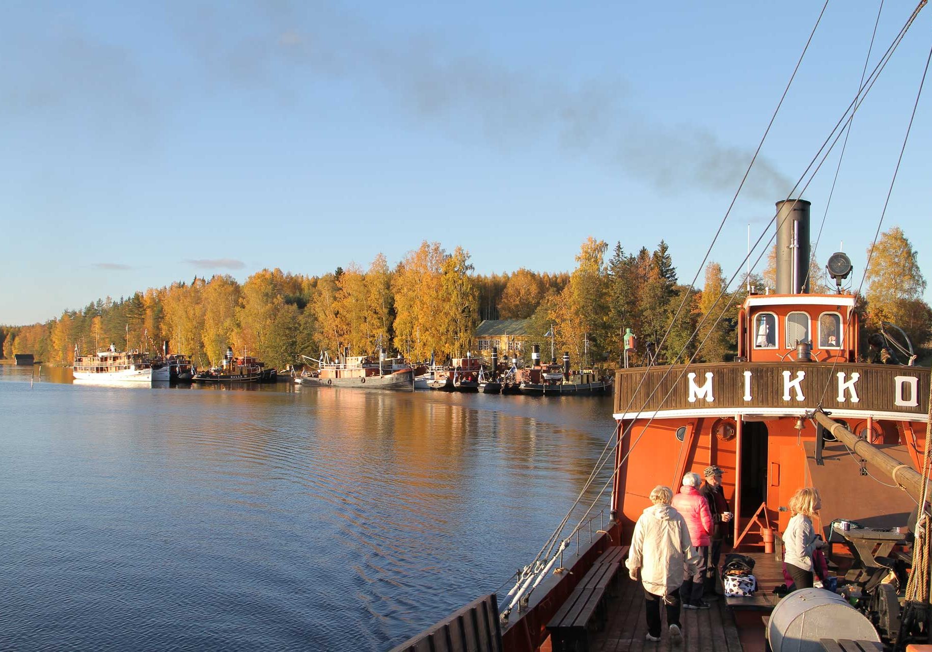 Kuvassa Mikko-laiva kuvattuna syksyisessä aurinkoisessa maisemassa risteilemässä Pihlajavedellä. Taustalla Laukansaaren vanha koulu, jonka laivalaituriin on kiinnittynyt laivoja. Koululla sijaitsee yksi Suomen Höyrypursiseuran tukikohdista.