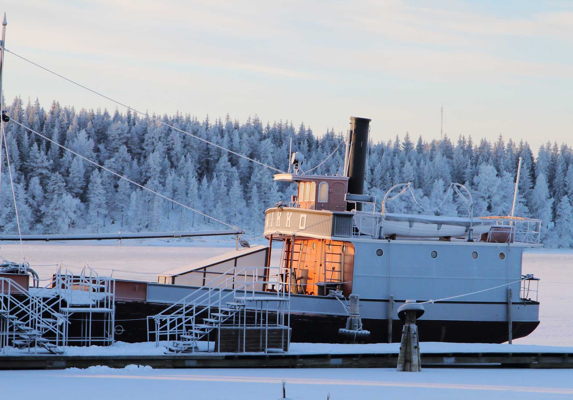 Kuvassa on Mikko-laiva kuvattuna talvipäivä huurteen kuorruttamana omassa kotilaiturissa Riihisaaressa. Aurinko välkähtää kuvassa siten, että auringonsäteet osuvat laivan siltarakenteeseen ja ohjaamoon.